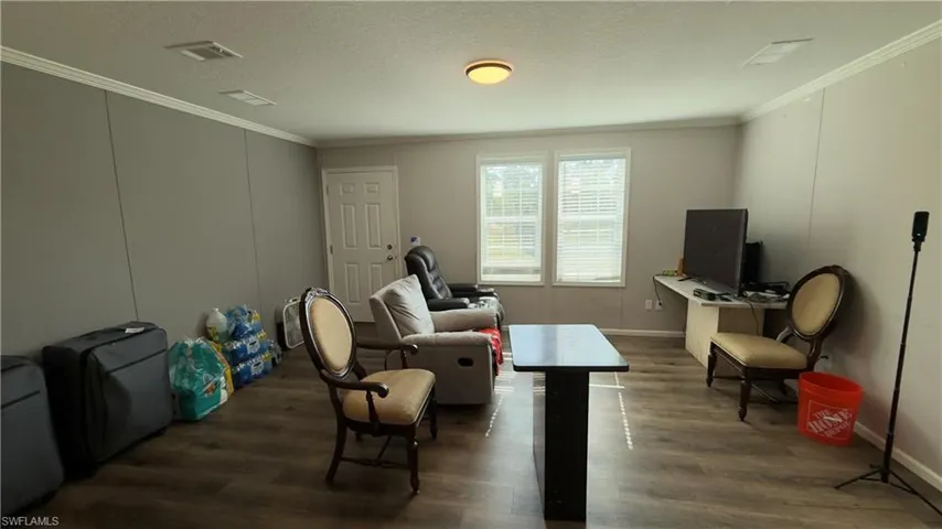 Living area with a textured ceiling, wood finished floors, crown molding, and a desk