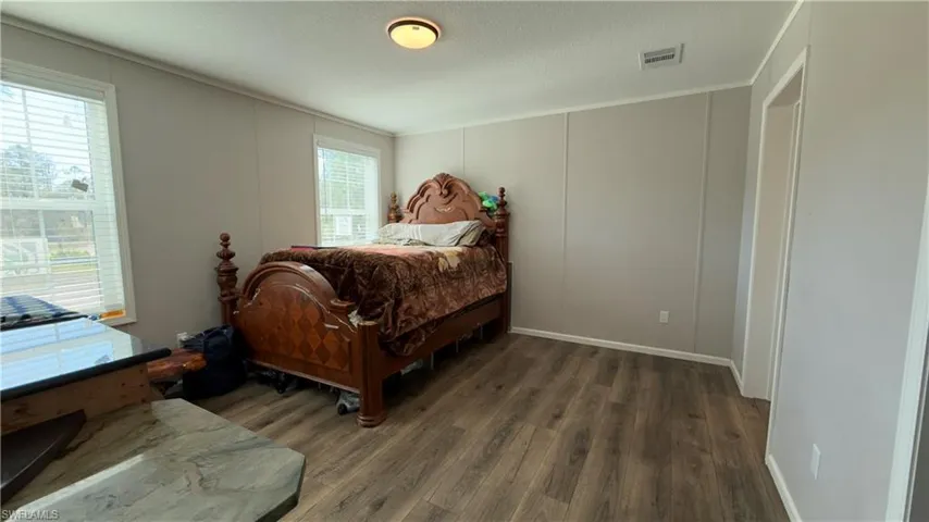 Bedroom featuring a decorative wall, multiple windows, dark wood-style flooring, and a textured ceiling