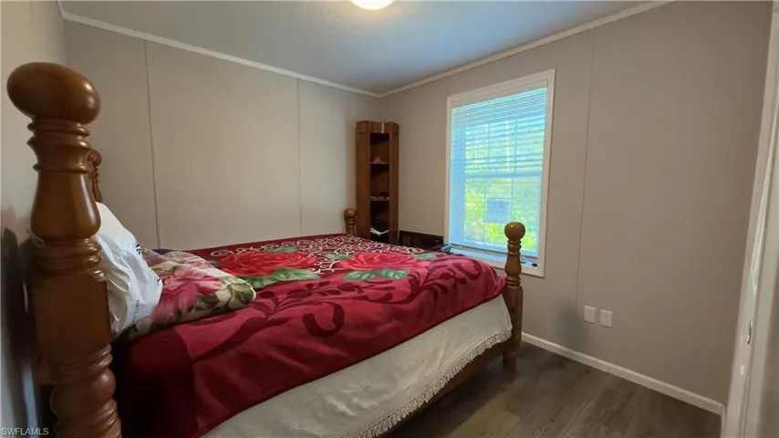 Bedroom with dark wood-type flooring, crown molding, and a decorative wall