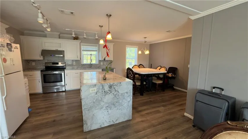 Kitchen with ornamental molding, freestanding refrigerator, stainless steel range with electric stovetop, hanging light fixtures, and white cabinets