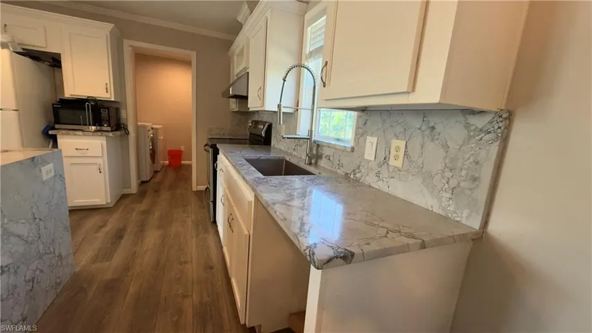 Kitchen with black appliances, washing machine and dryer, ornamental molding, dark wood-style floors, and light stone counters