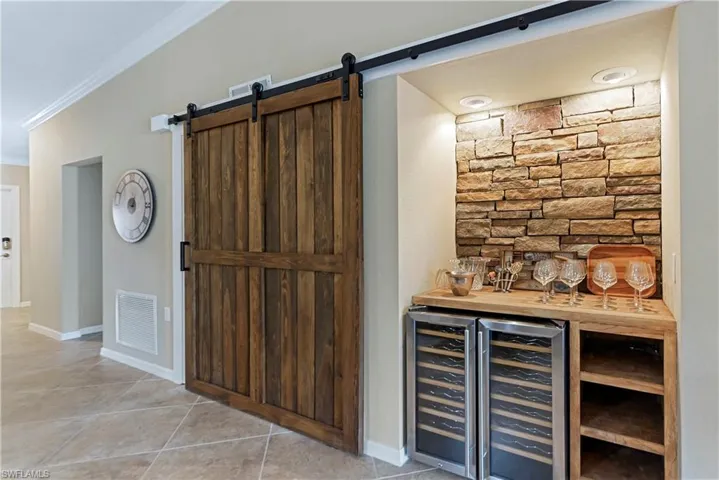 Bar featuring wood counters, wine cooler, a barn door, light tile patterned floors, and ornamental molding