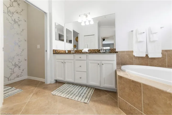 Bathroom with tile patterned flooring, vanity, ornamental molding, and tiled tub