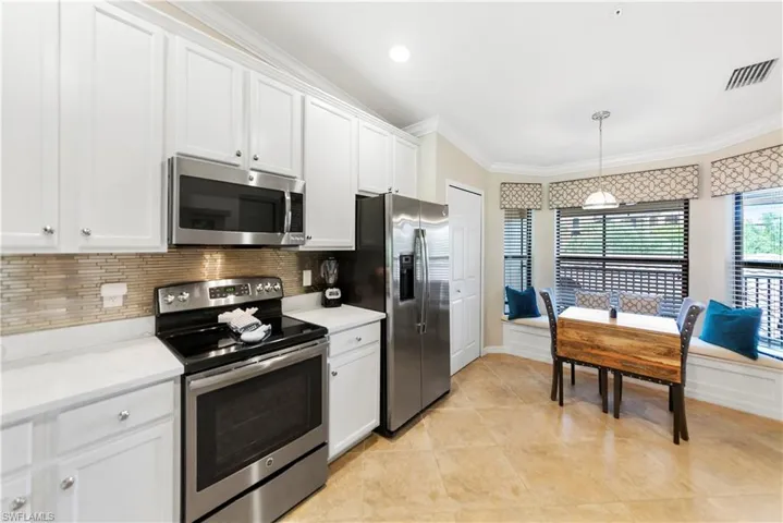 Kitchen with appliances with stainless steel finishes, backsplash, crown molding, pendant lighting, and white cabinetry