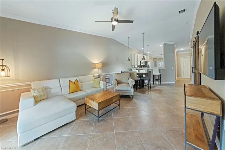 Tiled living room with lofted ceiling, a barn door, ceiling fan, and crown molding