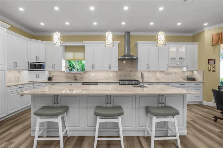 Kitchen with large center island (10'x4'), plentiful custom cabinets for storage, natural gas range with hood ventilated to outside, luxury vinyl flooring, LED ceiling lighting and 3 hanging pendants for bar stool dining. Note center island has second sink.