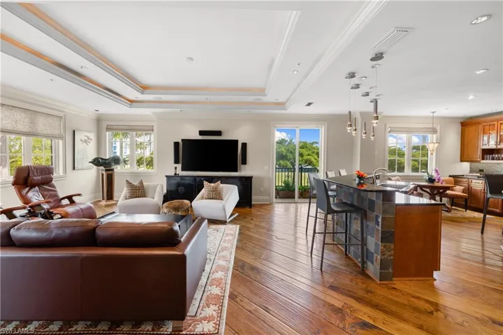 Open-concept living space featuring wood flooring, a tray ceiling with recessed lighting, and large windows and a balcony