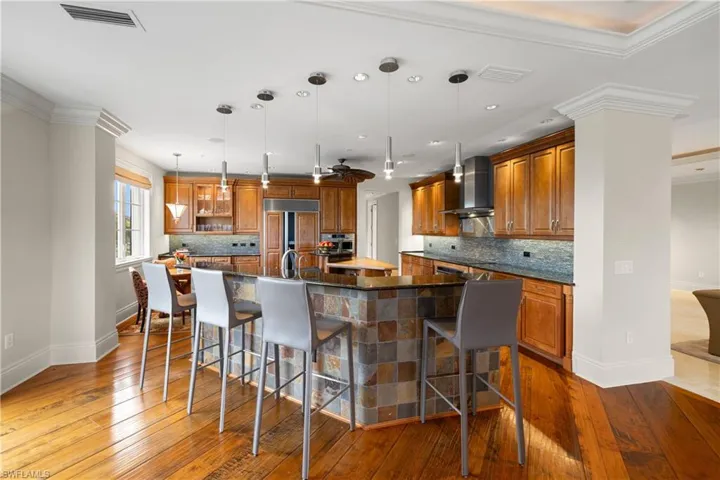 Open-concept kitchen featuring hand-carved hickory wood flooring, an island with countertop seating, stainless steel appliances, wood cabinetry, and a tile backsplash