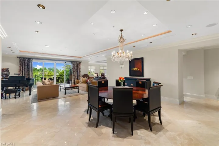Open-concept living and dining area featuring marble flooring, a tray ceiling with recessed lighting, and a crystal chandelier
