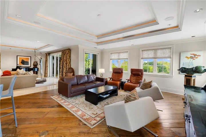 Spacious living area featuring wide-plank wood flooring, decorative tray ceilings with recessed lighting, and multiple large windows