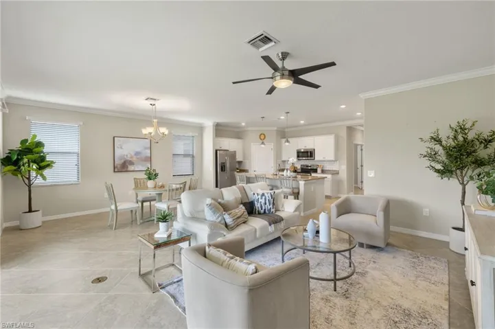 Living room featuring ornamental molding, light tile floors, and ceiling fan with notable chandelier