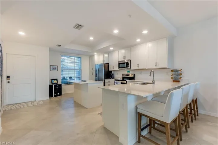 Kitchen with white cabinets, appliances with stainless steel finishes, a kitchen island, kitchen peninsula, and a breakfast bar area