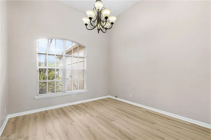 Empty room with a chandelier, light wood-style flooring, and vaulted ceiling