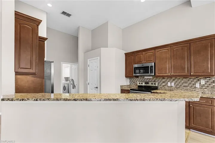 Kitchen with stainless steel appliances, light stone counters, a high ceiling, and tasteful backsplash
