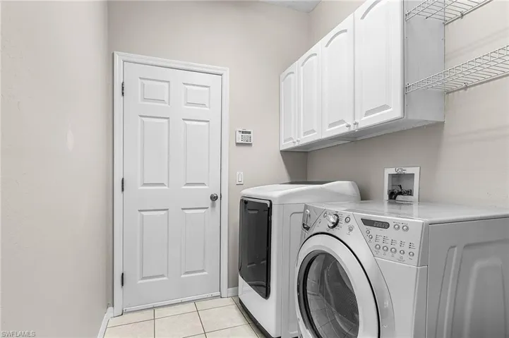 Laundry area featuring cabinet space, light tile patterned flooring, and washing machine and dryer