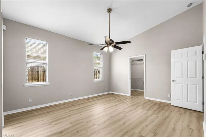 Unfurnished bedroom with lofted ceiling, a spacious closet, light wood-style flooring, and ceiling fan