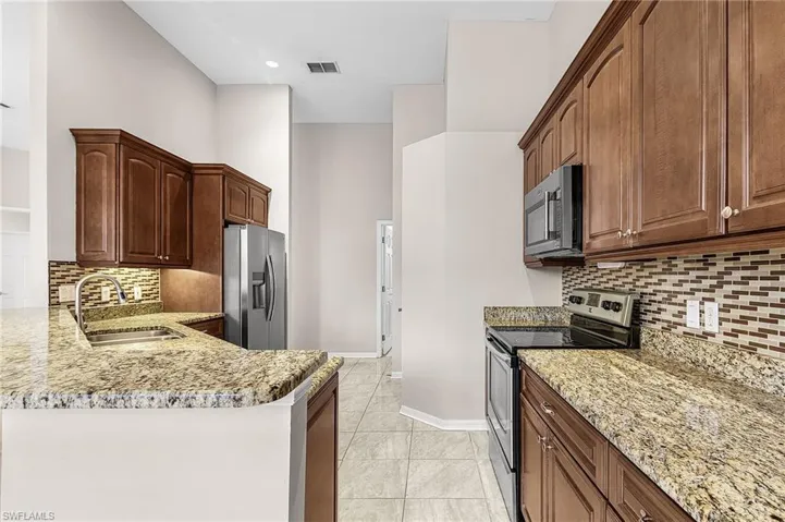 Kitchen featuring stainless steel appliances, light stone countertops, tasteful backsplash, a peninsula, and light tile patterned floors
