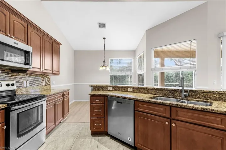 Kitchen featuring stainless steel appliances, light stone countertops, backsplash, a chandelier, and vaulted ceiling