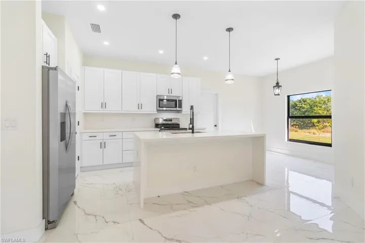 Kitchen with white cabinetry, light marble finish floors, light stone counters, stainless steel appliances, and hanging light fixtures