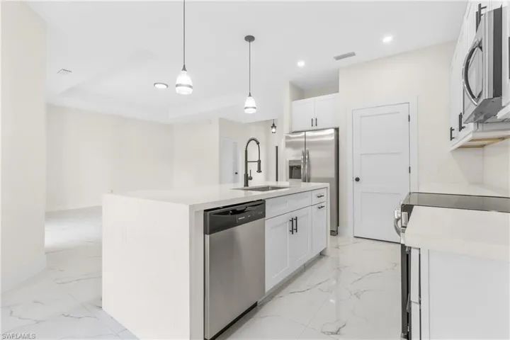 Kitchen featuring recessed lighting, stainless steel appliances, hanging light fixtures, light stone countertops, and white cabinetry