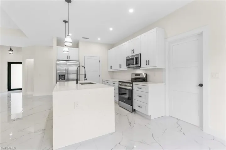 Kitchen with appliances with stainless steel finishes, white cabinetry, light stone countertops, decorative light fixtures, and a kitchen island with sink
