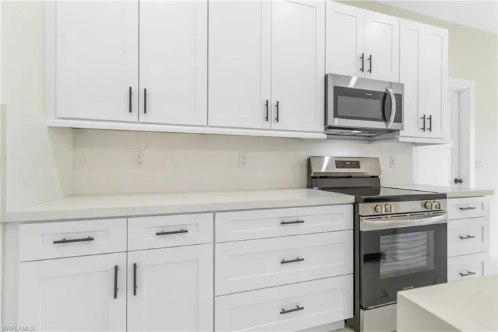 Kitchen featuring appliances with stainless steel finishes, white cabinets, light stone countertops, and decorative backsplash