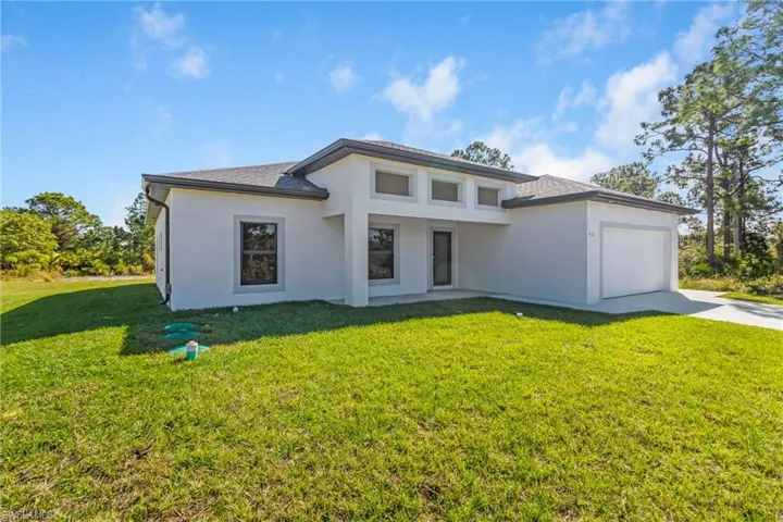 Prairie-style home featuring a front lawn, an attached garage, concrete driveway, and stucco siding