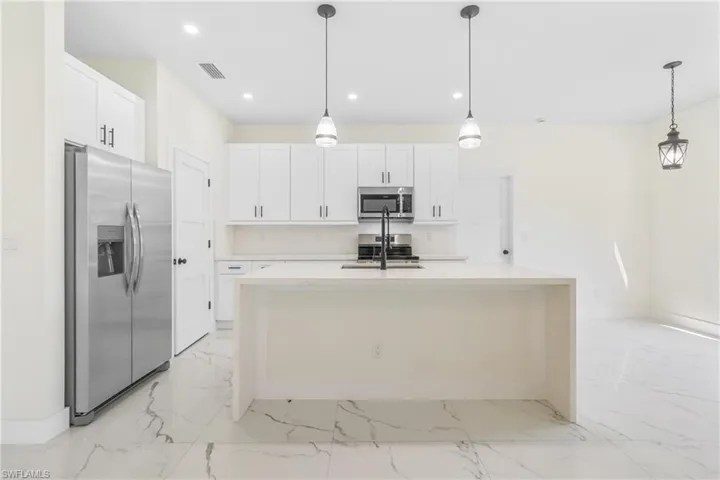 Kitchen featuring light marble finish floors, appliances with stainless steel finishes, white cabinets, light stone counters, and recessed lighting