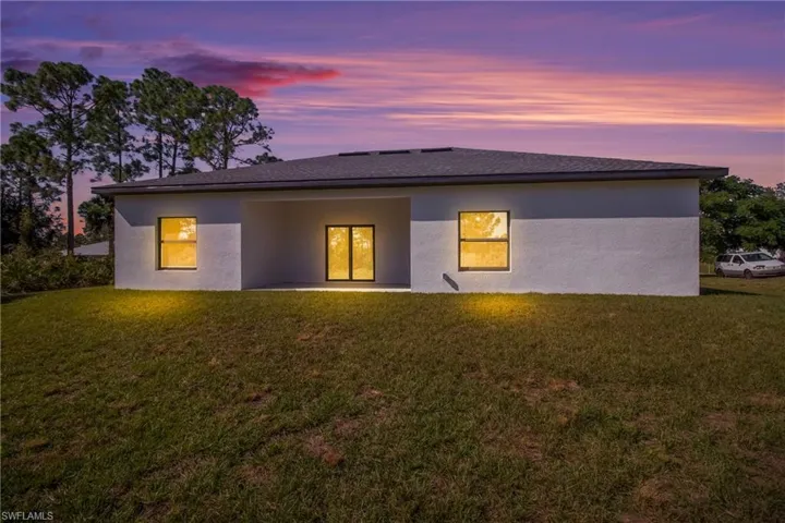 Back of property at dusk featuring a yard, a patio area, stucco siding, and roof with shingles