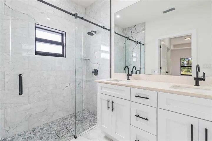 Full bath with double vanity, a marble finish shower, and light marble finish flooring