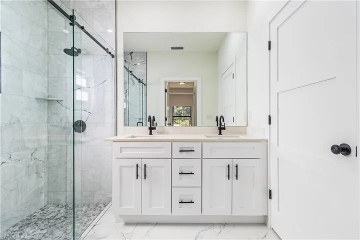 Full bath with light marble finish floors, double vanity, and a marble finish shower