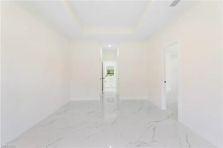 Unfurnished room featuring a raised ceiling and light marble finish floors