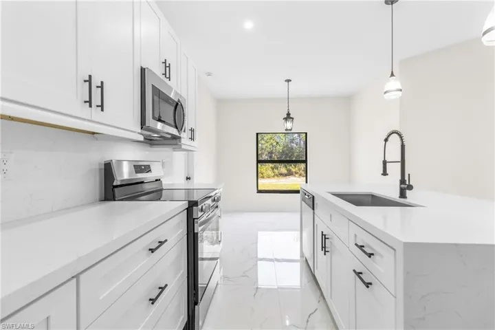 Kitchen featuring stainless steel appliances, white cabinetry, light stone countertops, decorative light fixtures, and recessed lighting