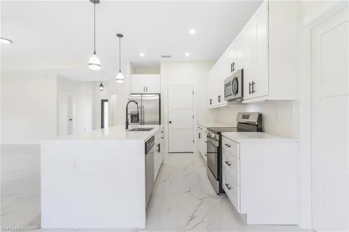 Kitchen featuring appliances with stainless steel finishes, pendant lighting, white cabinetry, recessed lighting, and light marble finish flooring
