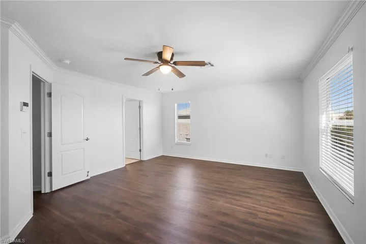 Unfurnished bedroom with crown molding, dark wood-style flooring, and a ceiling fan
