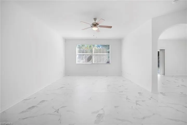 Unfurnished room with arched walkways, ceiling fan, and light marble finish flooring