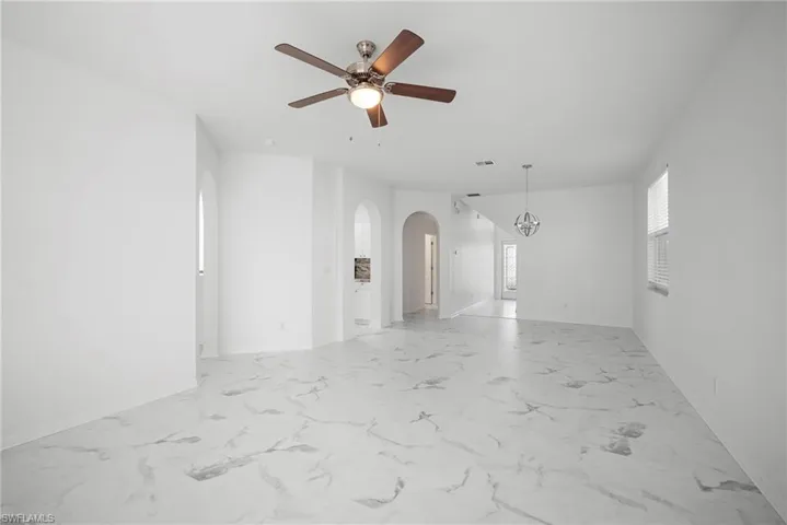 Empty room featuring arched walkways, a ceiling fan, and light marble finish flooring