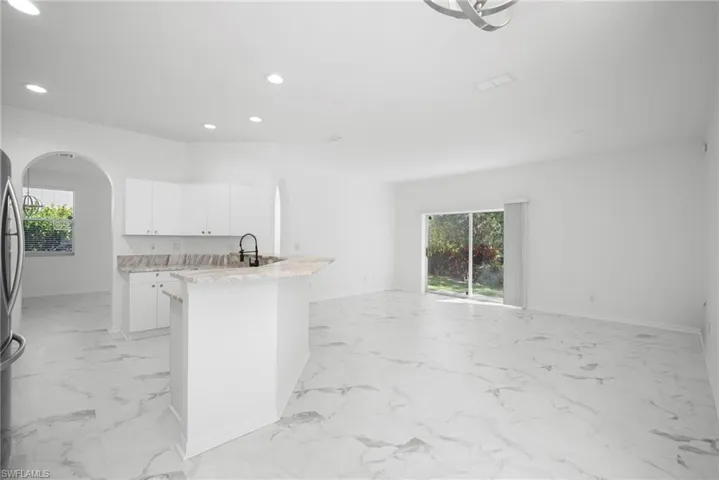 Kitchen with white cabinetry, arched walkways, recessed lighting, freestanding refrigerator, and light stone countertops