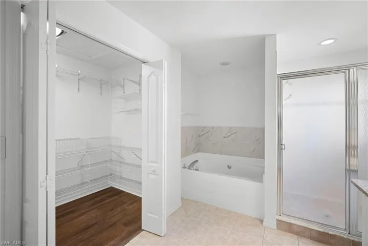 Bathroom with a spacious closet, a garden tub, a stall shower, and light tile patterned floors