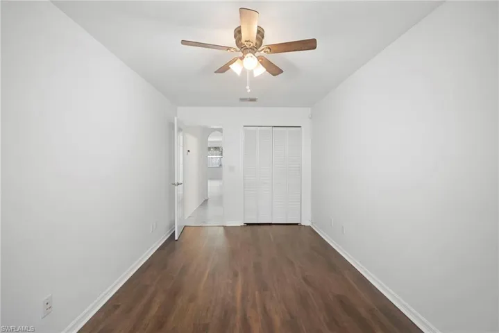 Unfurnished bedroom featuring a closet, dark wood-style flooring, ceiling fan, and arched walkways