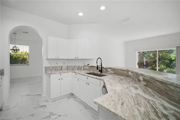 Kitchen featuring white cabinets, arched walkways, light stone counters, a peninsula, and light marble finish flooring