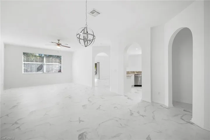 Unfurnished living room with arched walkways, suspended lighting, a ceiling fan, and light marble finish flooring