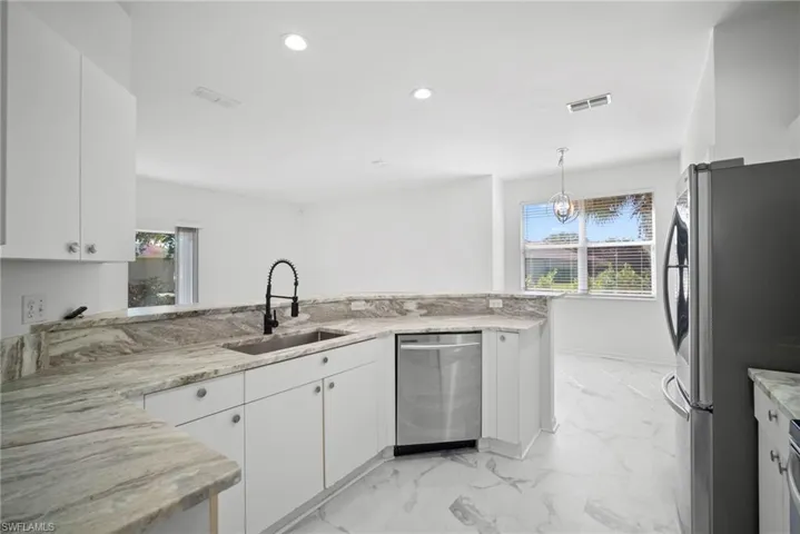 Kitchen with stainless steel appliances, white cabinets, decorative light fixtures, light stone countertops, and a peninsula