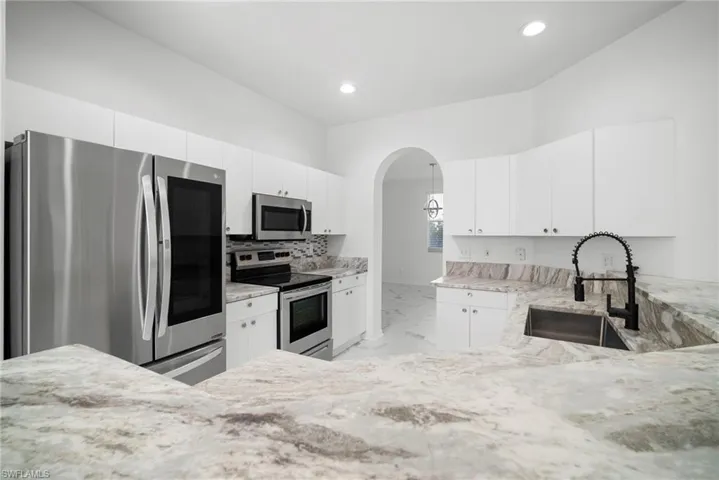 Kitchen featuring stainless steel appliances, arched walkways, white cabinetry, and light stone counters