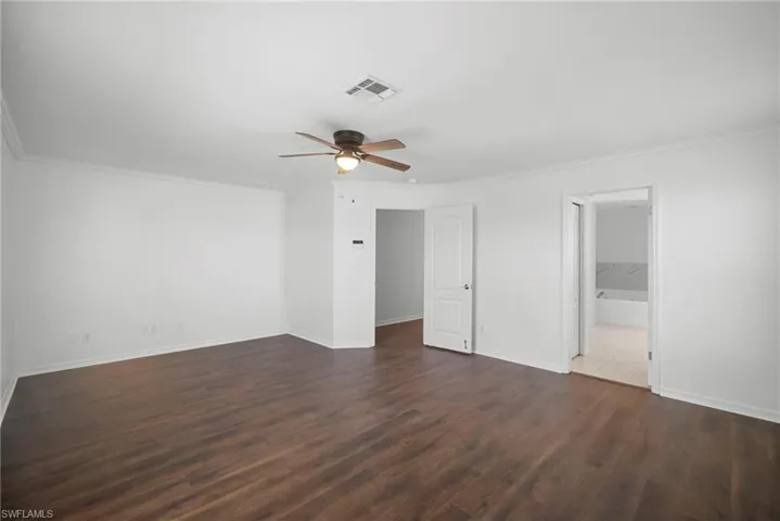 Unfurnished bedroom with ornamental molding, dark wood-style floors, ceiling fan, and connected bathroom