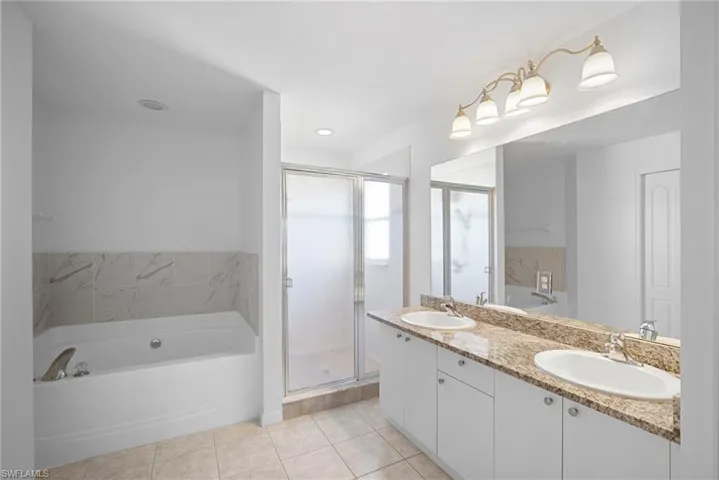 Full bath featuring a bath, double vanity, a shower stall, and light tile patterned flooring
