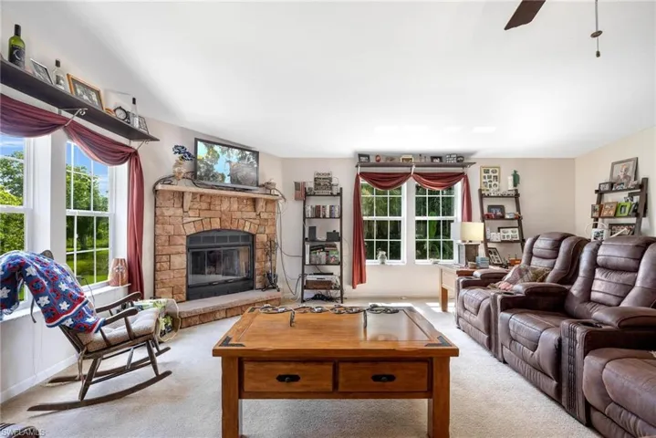 Living room featuring a stone fireplace, carpet flooring, and ceiling fan