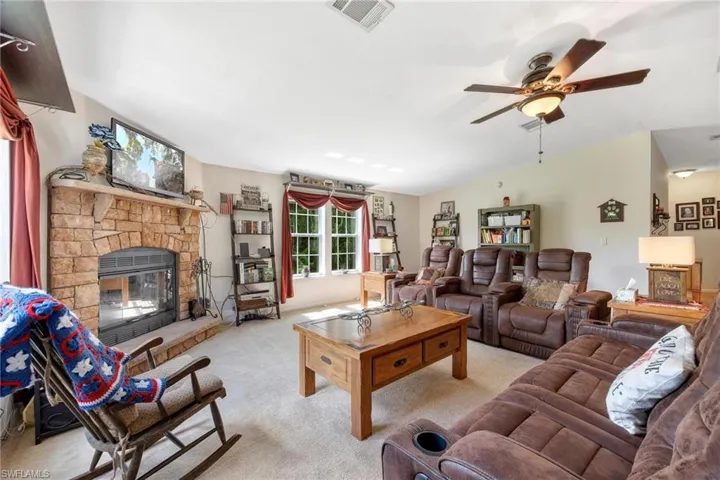 Living room with light colored carpet, a stone fireplace, and ceiling fan