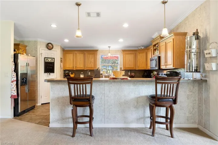 Kitchen with light colored carpet, appliances with stainless steel finishes, a kitchen bar, and kitchen peninsula