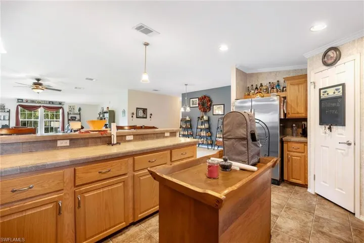 Kitchen with ceiling fan, stainless steel refrigerator with ice dispenser, pendant lighting, a center island, and light tile patterned floors